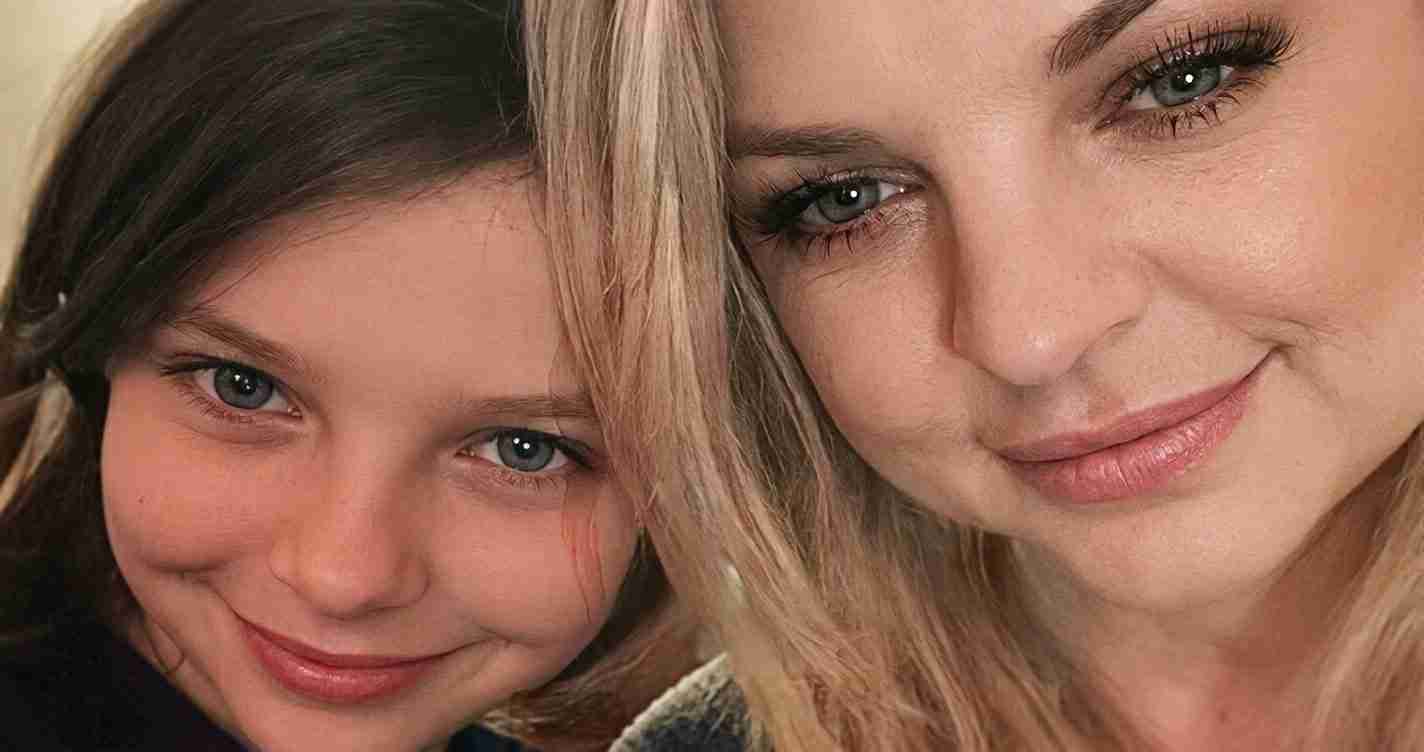 Close-up selfie of two smiling people: a girl with dark hair and blue eyes on the left, and a blonde woman on the right.]
