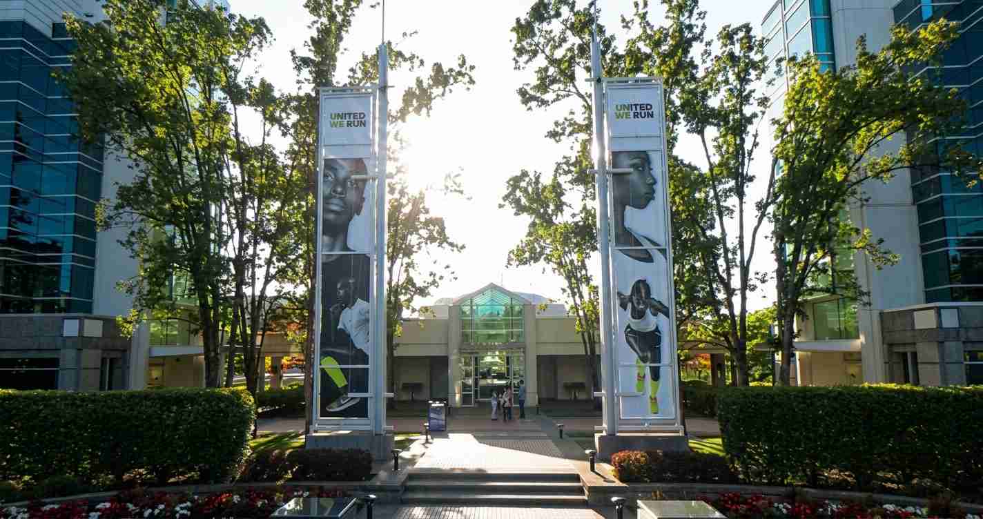 Campus plaza with two tall banners that read 'UNITED WE RUN' and feature athletes, sun behind trees.