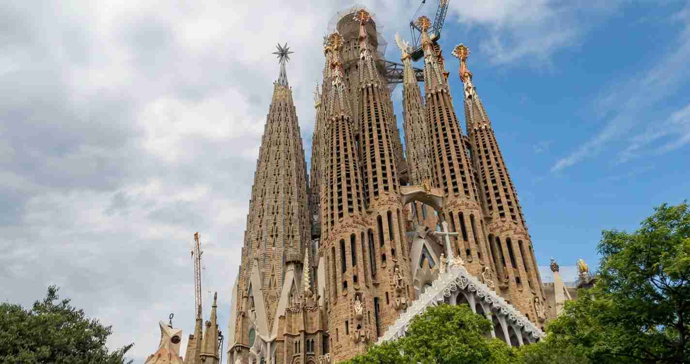 Sagrada Família in Barcelona with tall stone spires and construction cranes against a partly cloudy sky