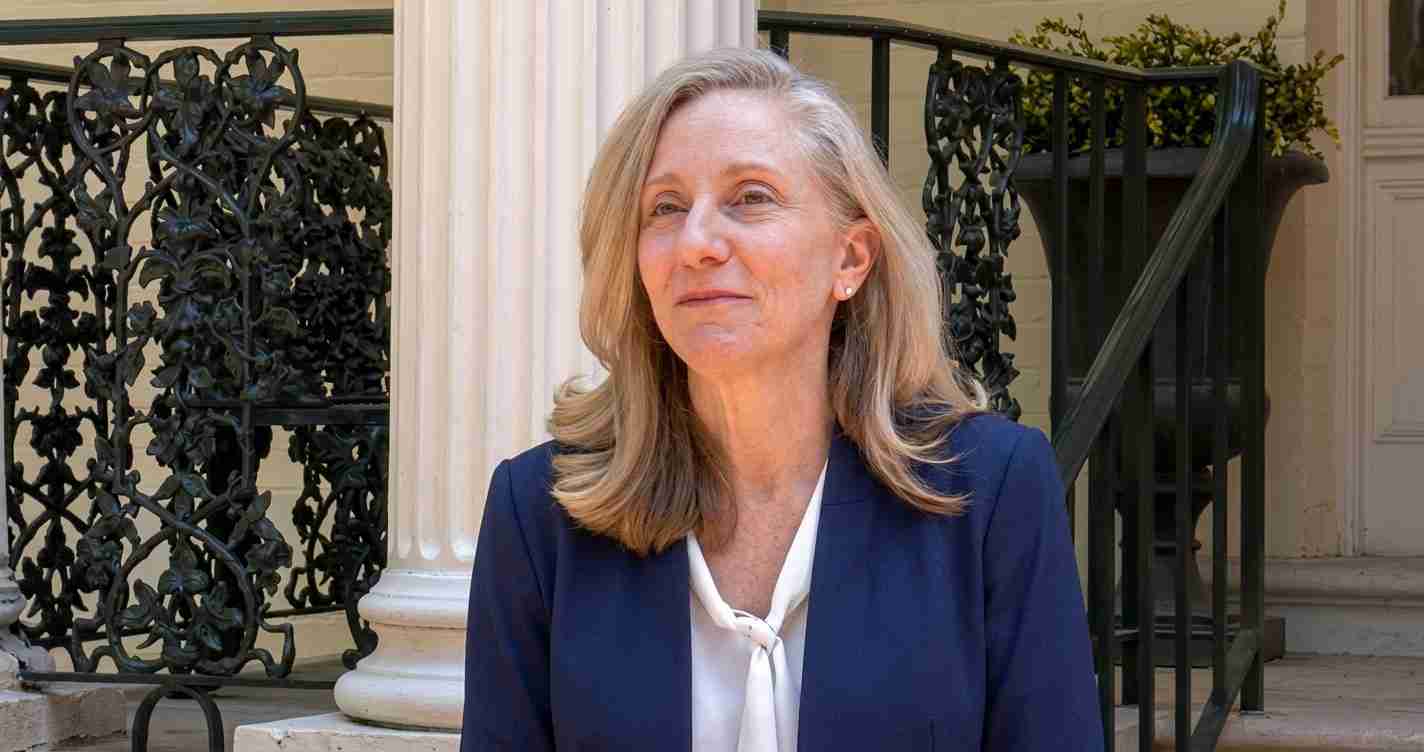 Portrait of a woman in a navy blazer and white blouse standing outside a columned building with decorative iron railings nearbye.