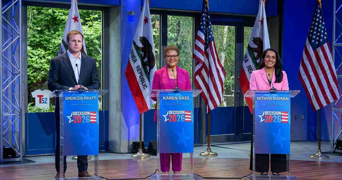 Three candidates stand at podiums on a blue debate stage with flags behind them, promoting Decision 2026.