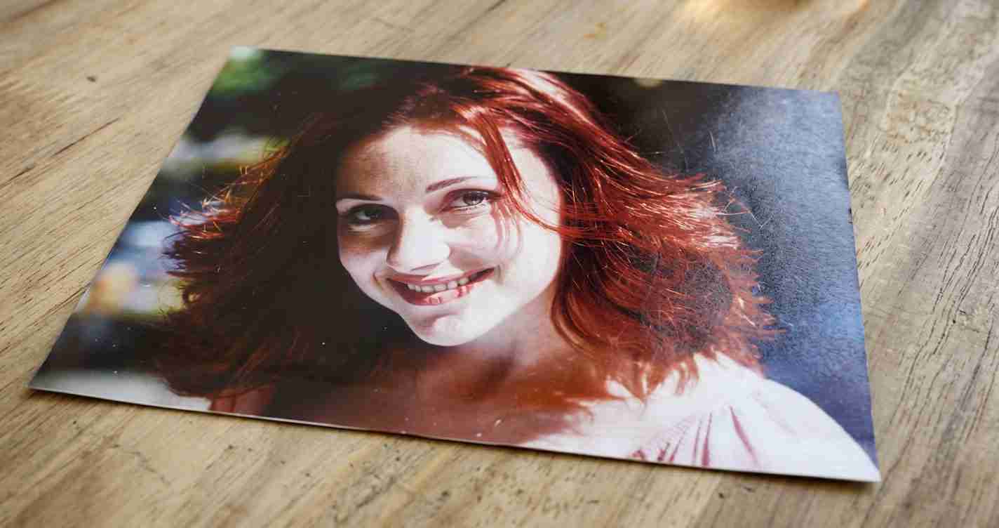 A glossy print of a smiling woman with red hair lying on a wooden surface.
