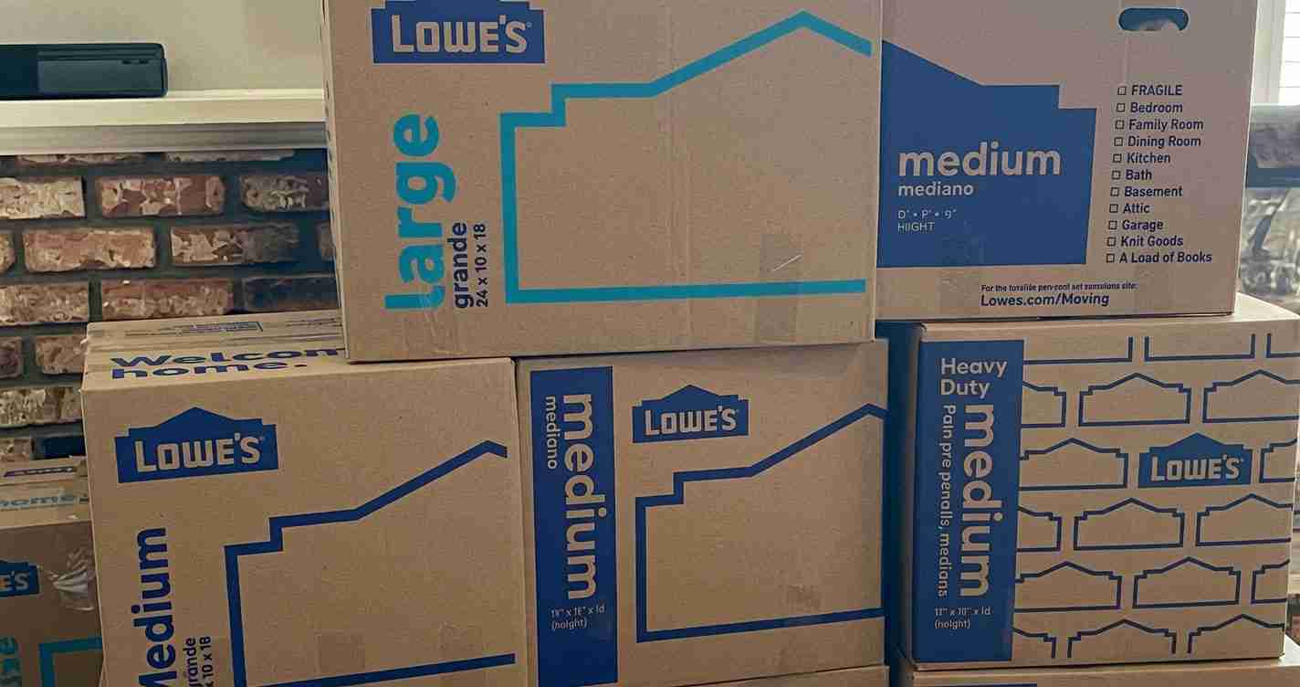 Stacked Lowe's moving boxes labeled 'Medium' and 'medium' with blue graphic lines, ready for moving or storage in a room.