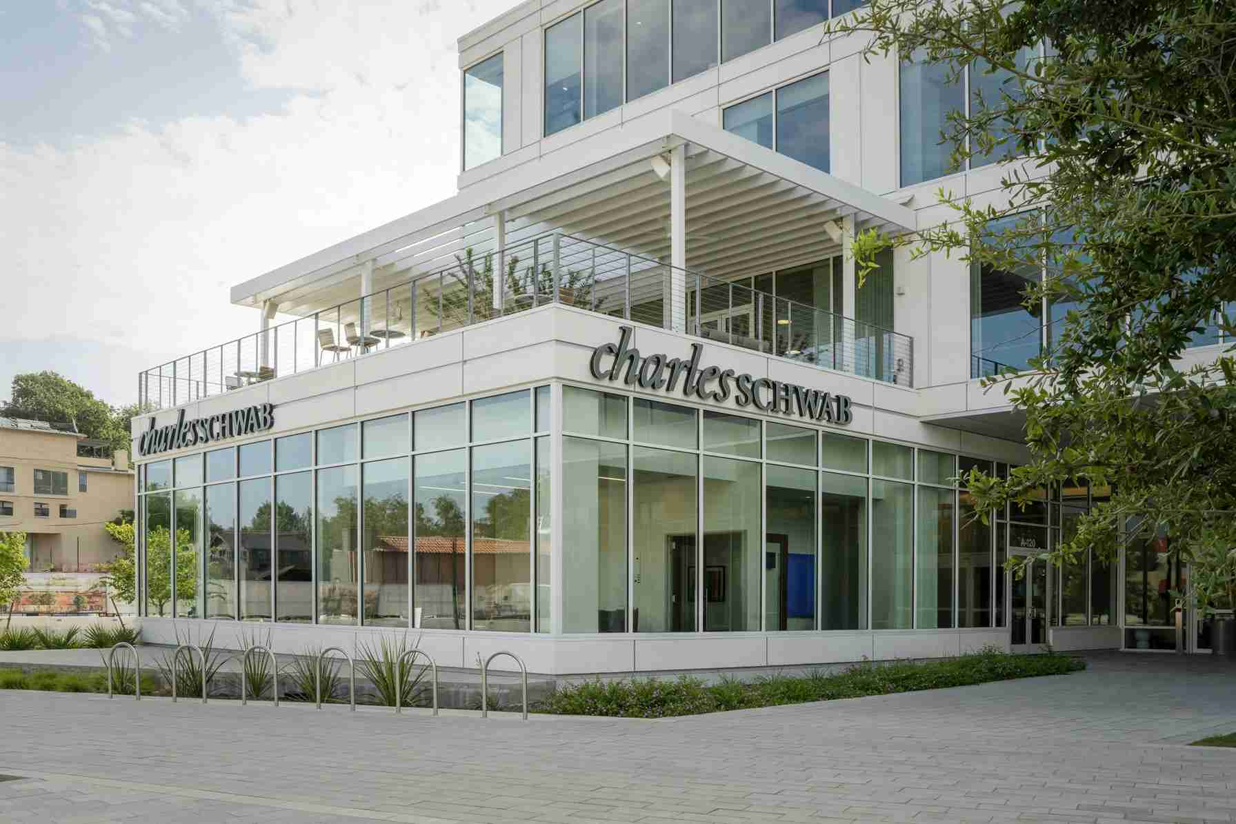 Exterior view of a modern Charles Schwab office building with glass walls and an outdoor terrace on the second level