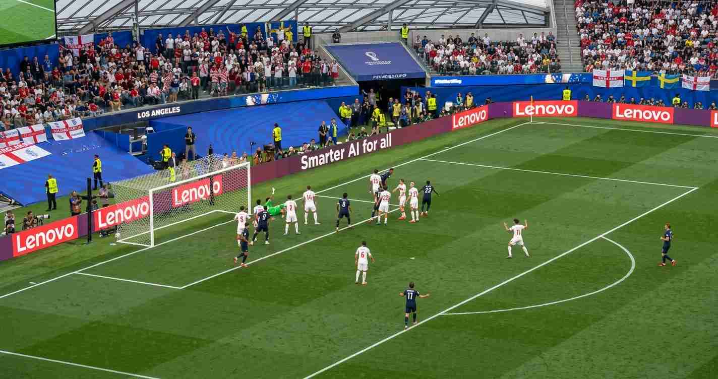 Soccer match near the goal with white-clad attackers and dark-clad defenders as fans watch from the stands and Lenovo ads line the pitch edge