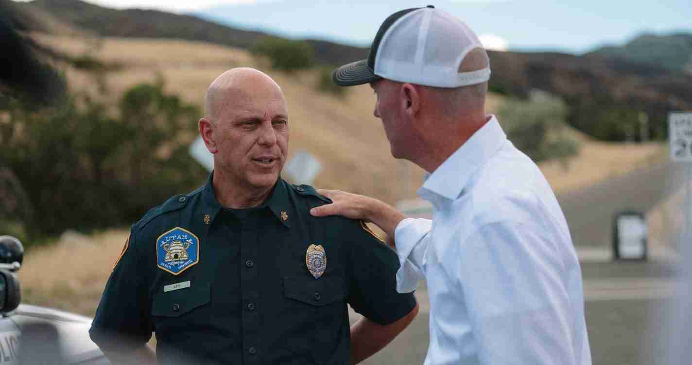 Two men stand by a roadside: a uniformed officer and a civilian talking seriously.