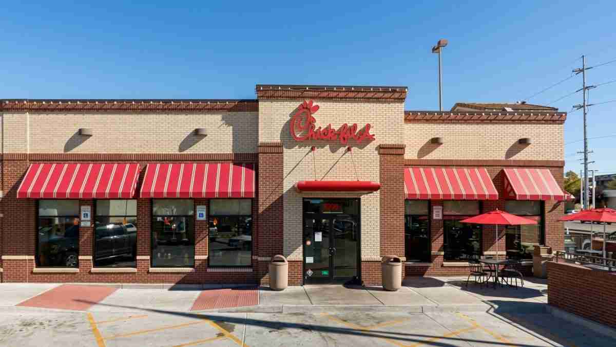 Chick-fil-A restaurant exterior with red striped awnings and outdoor seating under red umbrellas.