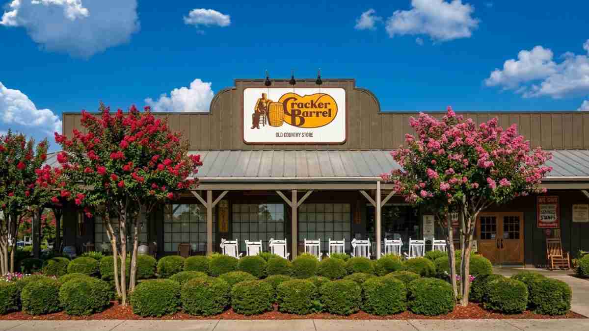 Cracker Barrel Old Country Store storefront with pink flowering trees and white rocking chairs on the porch under a blue sky: inviting country setting