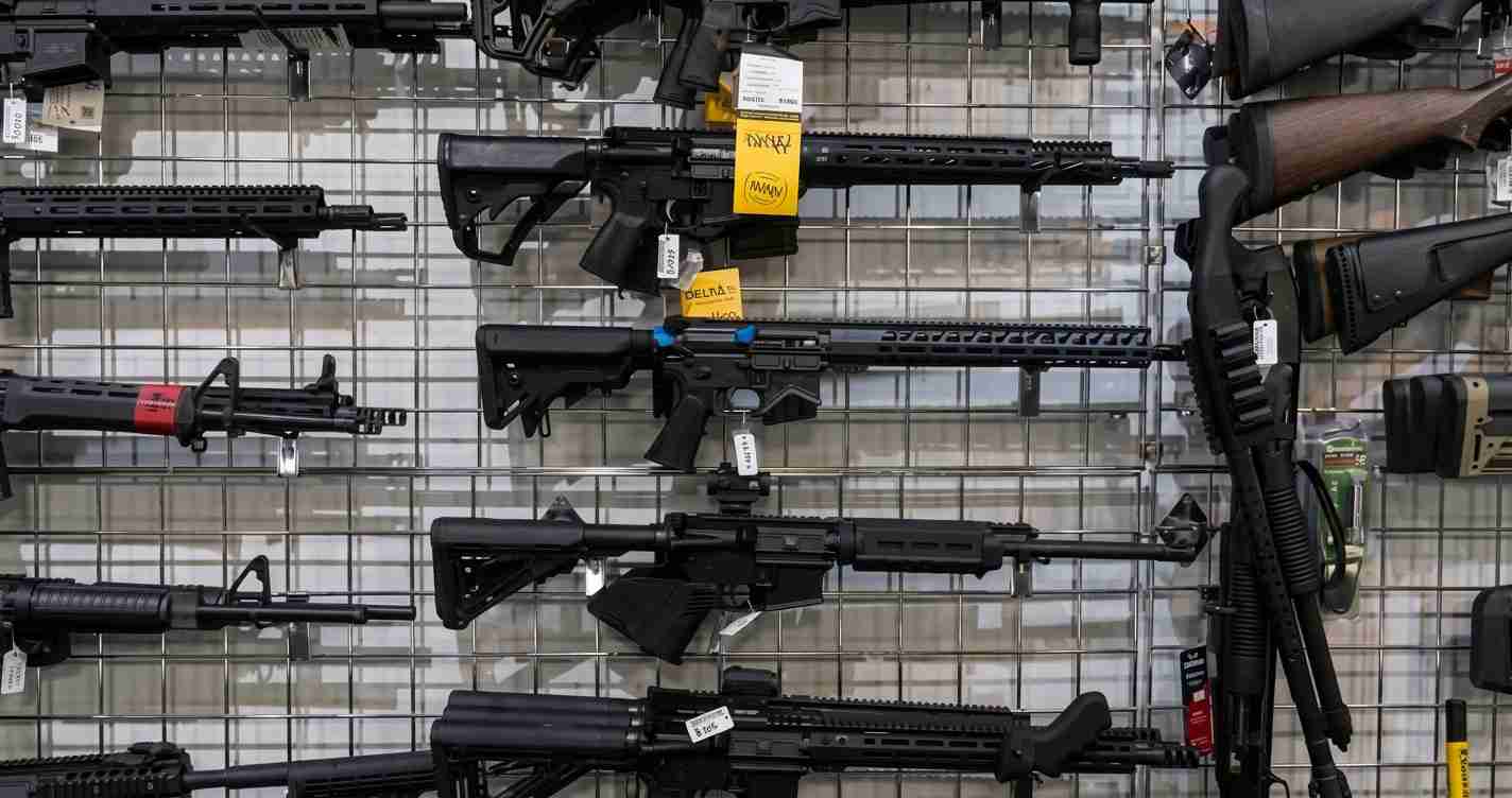 Row of semi-automatic rifles mounted on a grid wall in a gun shop, price tags visible.