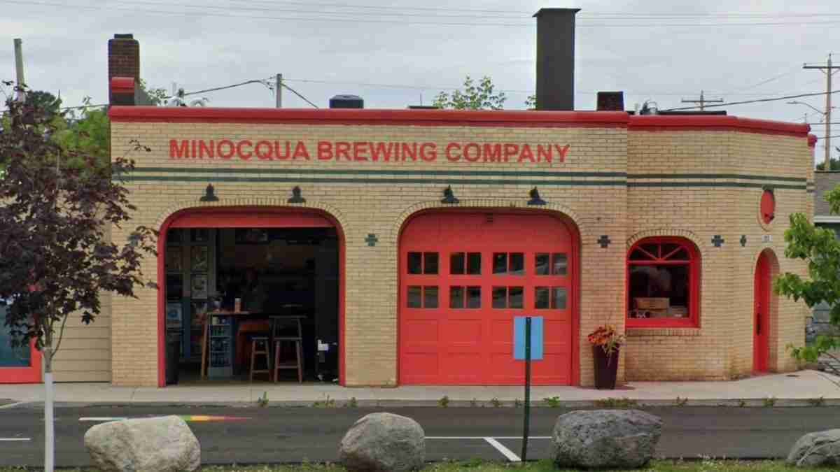 Brick brewery building labeled 'MINOCQUA BREWING COMPANY' with red doors and arched entryways, street-facing storefront and windows.