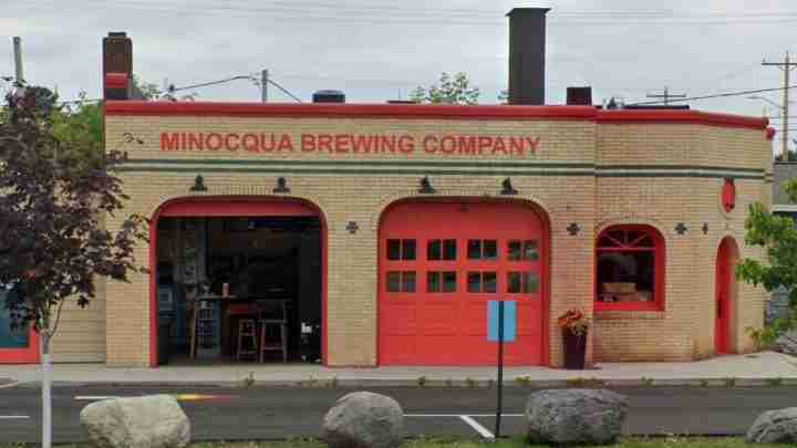 Brick brewery building labeled 'MINOCQUA BREWING COMPANY' with red doors and arched entryways, street-facing storefront and windows.