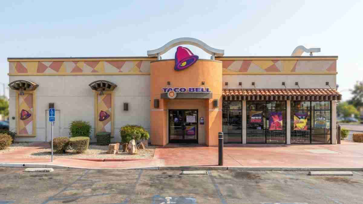 Exterior of a Taco Bell restaurant with orange curved entrance, purple bell logo, and large front windows.