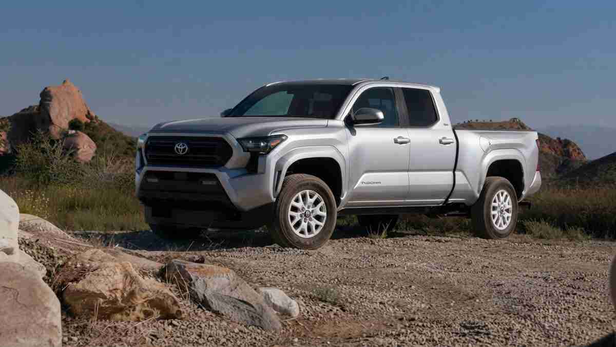 Silver Toyota Tacoma crew cab pickup parked on a rocky desert trail with hills in the distance, under a blue sky.