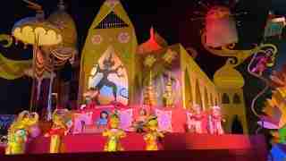 Vibrant festival float with colorful puppets in traditional costumes performing on a pink stage against a yellow, whimsical backdrop.