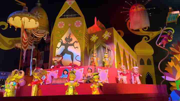 Vibrant festival float with colorful puppets in traditional costumes performing on a pink stage against a yellow, whimsical backdrop.