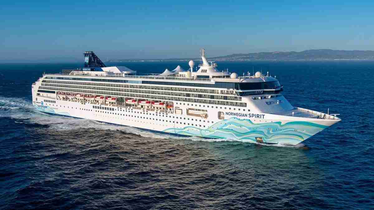 Large white cruise ship Norwegian Spirit sailing on blue sea, with turquoise wave artwork along the hull.