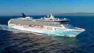 Large white cruise ship Norwegian Spirit sailing on blue sea, with turquoise wave artwork along the hull.