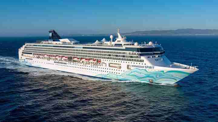 Large white cruise ship Norwegian Spirit sailing on blue sea, with turquoise wave artwork along the hull.