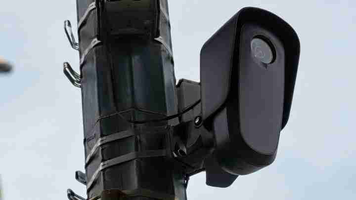 Close-up of a black surveillance camera mounted on a metal pole outdoors, monitoring traffic or surroundings.
