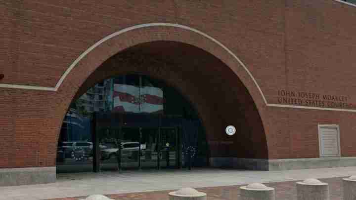 John Joseph Moakley United States Courthouse brick arch entrance with glass doors and a paved plaza in front.