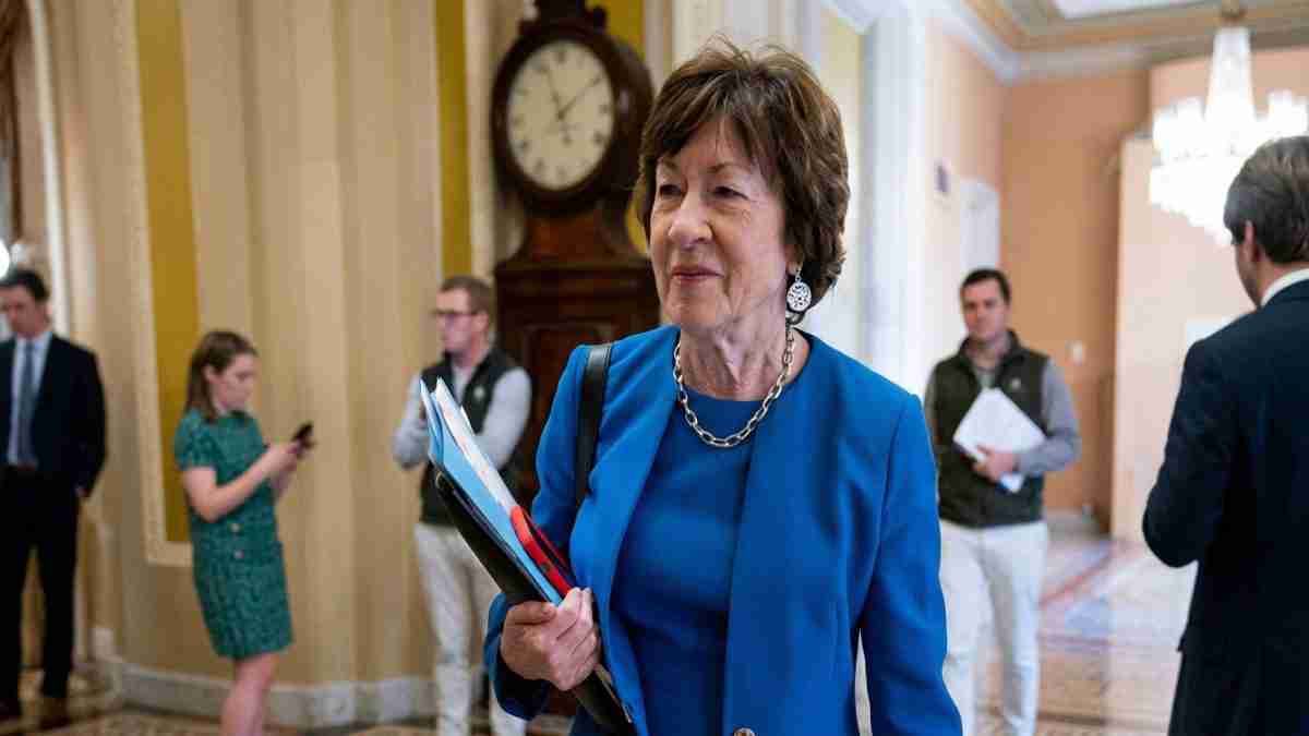 Woman in a blue blazer carrying folders walks through a marble lobby as others chat in the background.