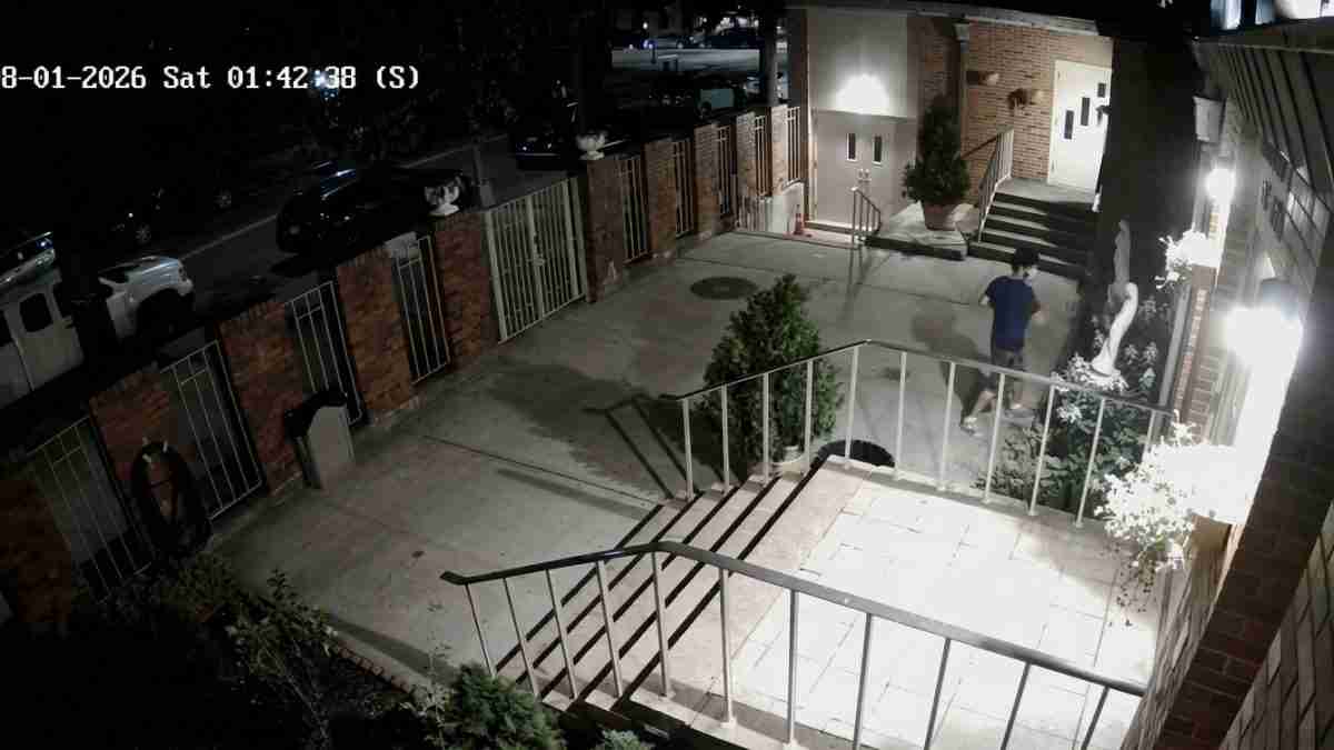Night exterior of a brick building with a person in a blue shirt walking toward the entrance; stairs and railing lead to a courtyard; timestamp 08-01-2026 Sat 01:42:38 (S).
