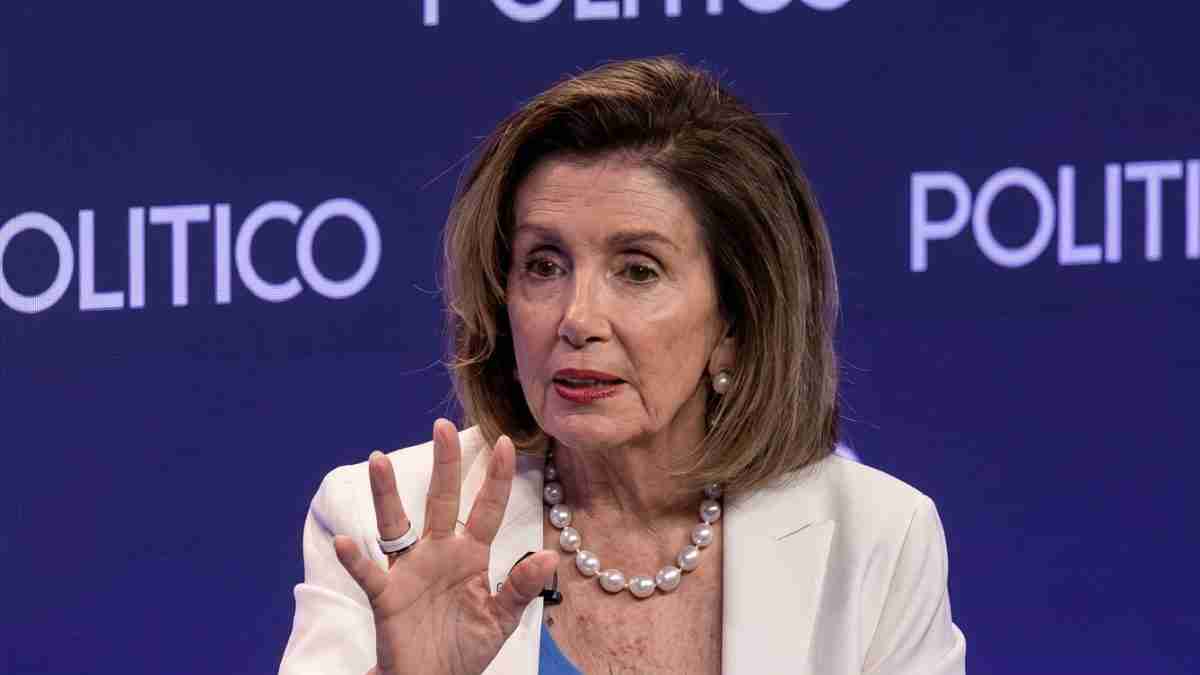 Woman speaking at a POLITICO event, raising her hand, wearing a white blazer and pearl necklace against a blue background.