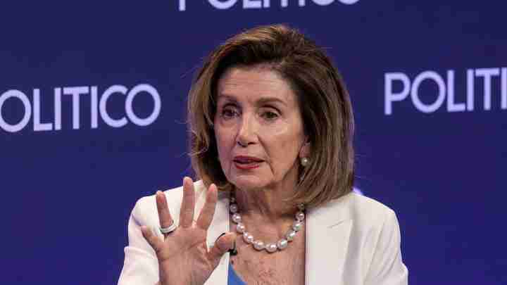 Woman speaking at a POLITICO event, raising her hand, wearing a white blazer and pearl necklace against a blue background.