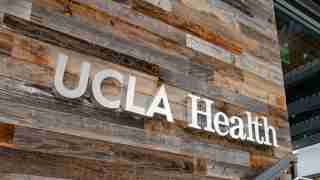 UCLA Health sign mounted on a wood-paneled wall outside a building.