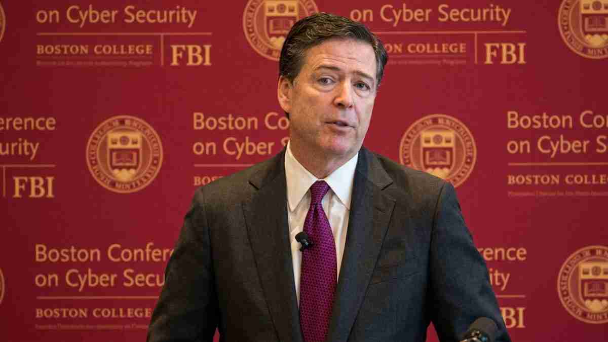 Man in a dark suit and red tie speaks at a cybersecurity conference, with a backdrop showing FBI and Boston College logos and the words 'Conference on Cyber Security'.