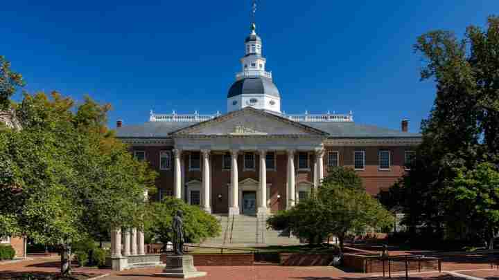 Front view of a brick university building with tall white columns, a domed cupola, and steps to the entrance on a sunny day.