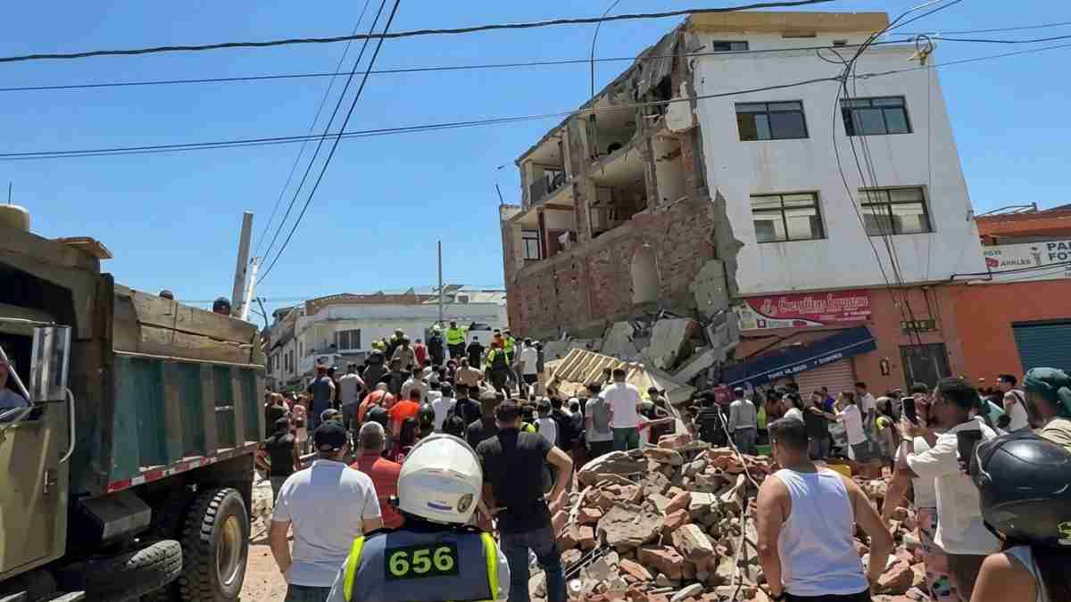 Street scene after a building collapse with rubble, a crowd of onlookers, and rescue workers in helmets coordinating work by a collapsed façade behind them.