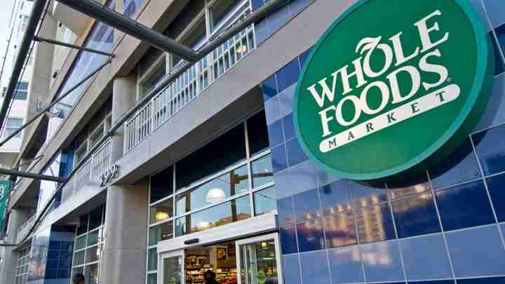 Whole Foods Market storefront with a large green circular sign on a blue tiled exterior