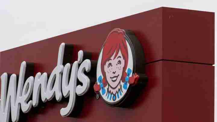 Wendy's restaurant sign on a burgundy facade, featuring the white script logo and the round cartoon girl emblem.