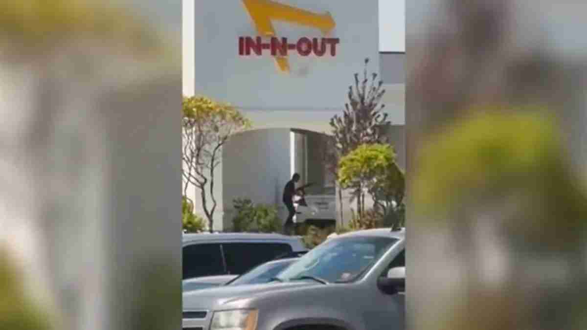 Person loading a delivery into a truck outside an In-N-Out restaurant, with a gray delivery vehicle and parked cars nearby.